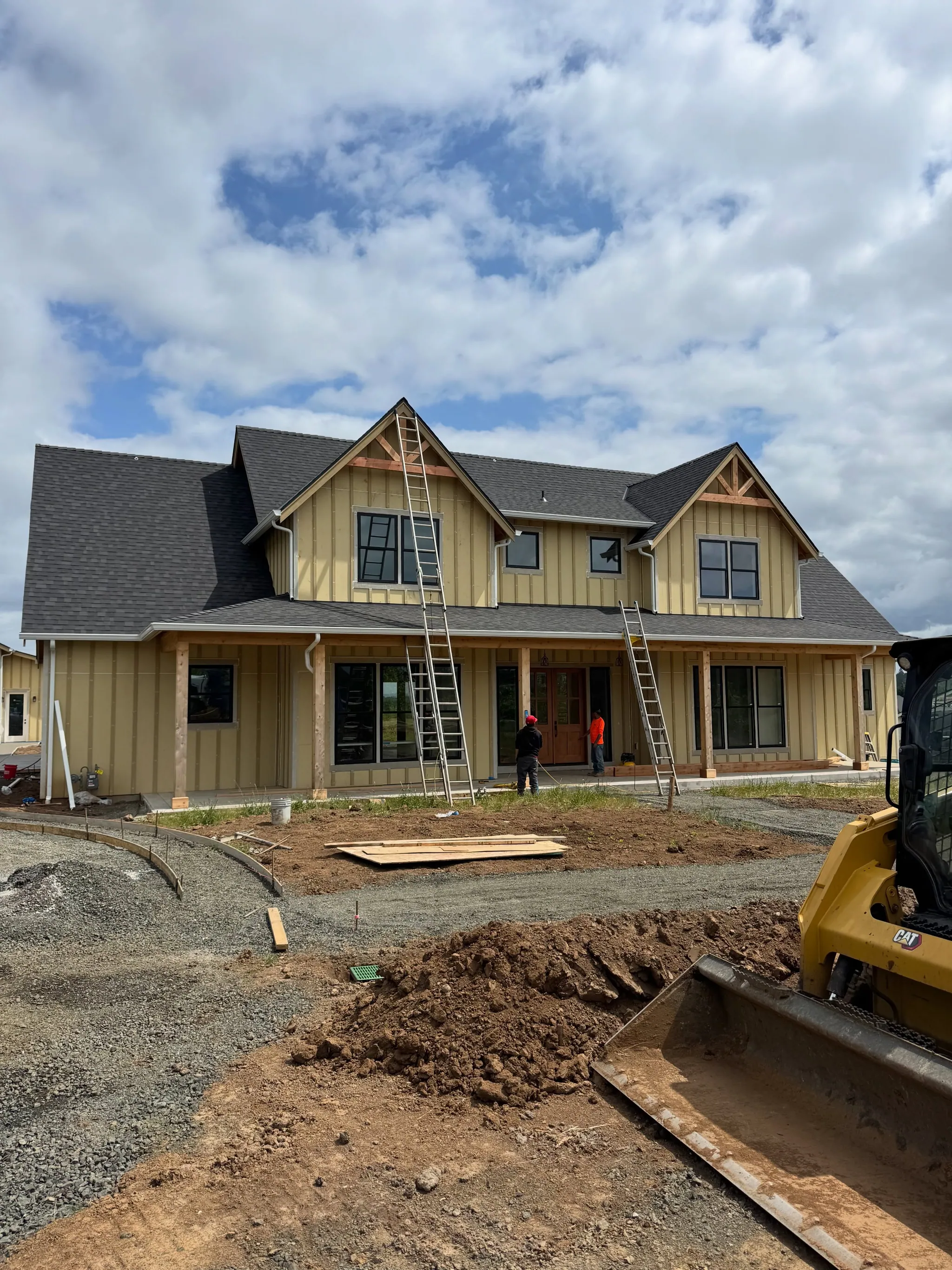 A board-and-batten farmhouse with a wide porch, ladders still up for the finish work
