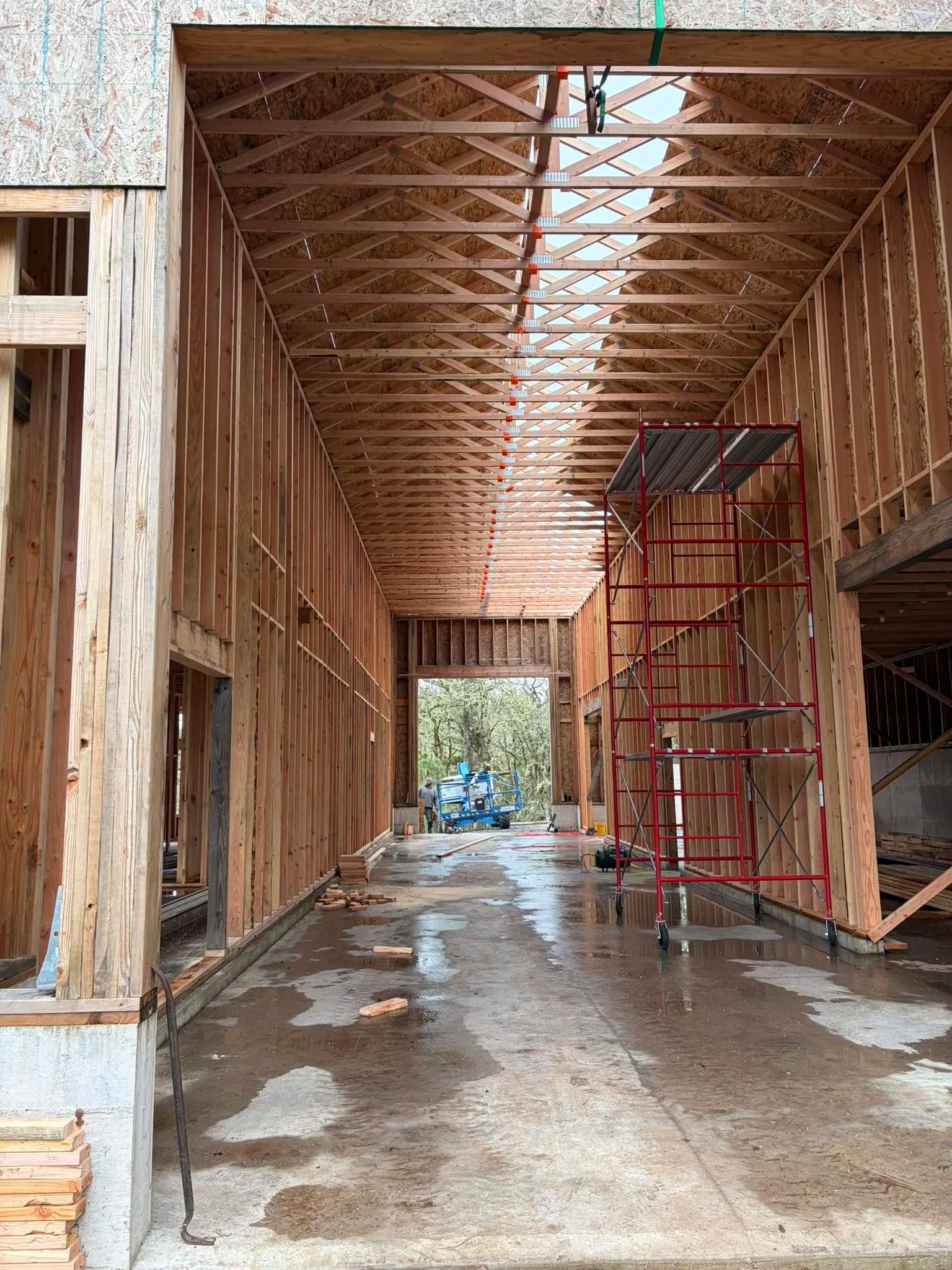 Inside a tall framed shop: open trusses overhead, scaffold and a wet slab