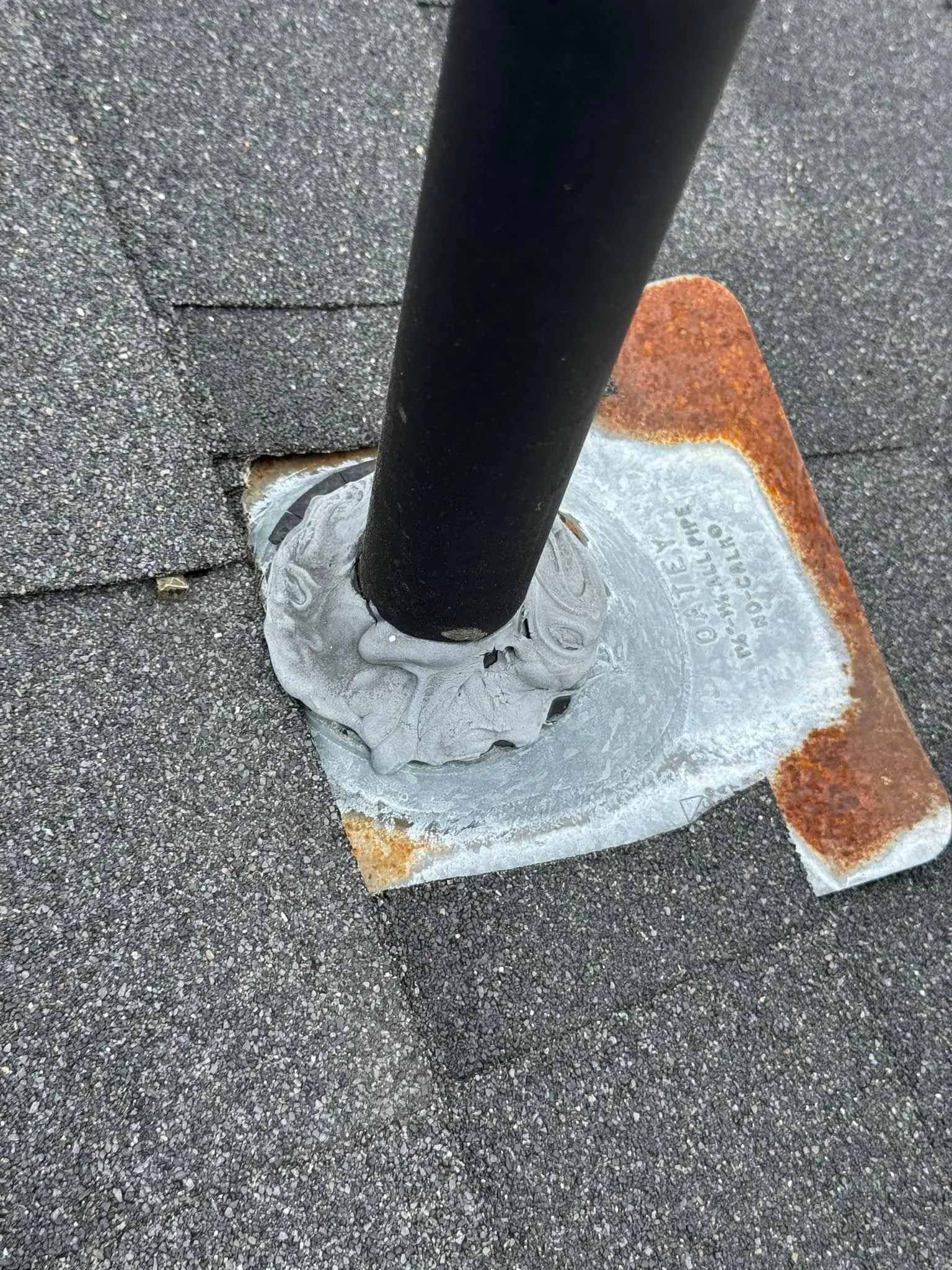 An old rusted pipe flashing on a shingle roof before replacement