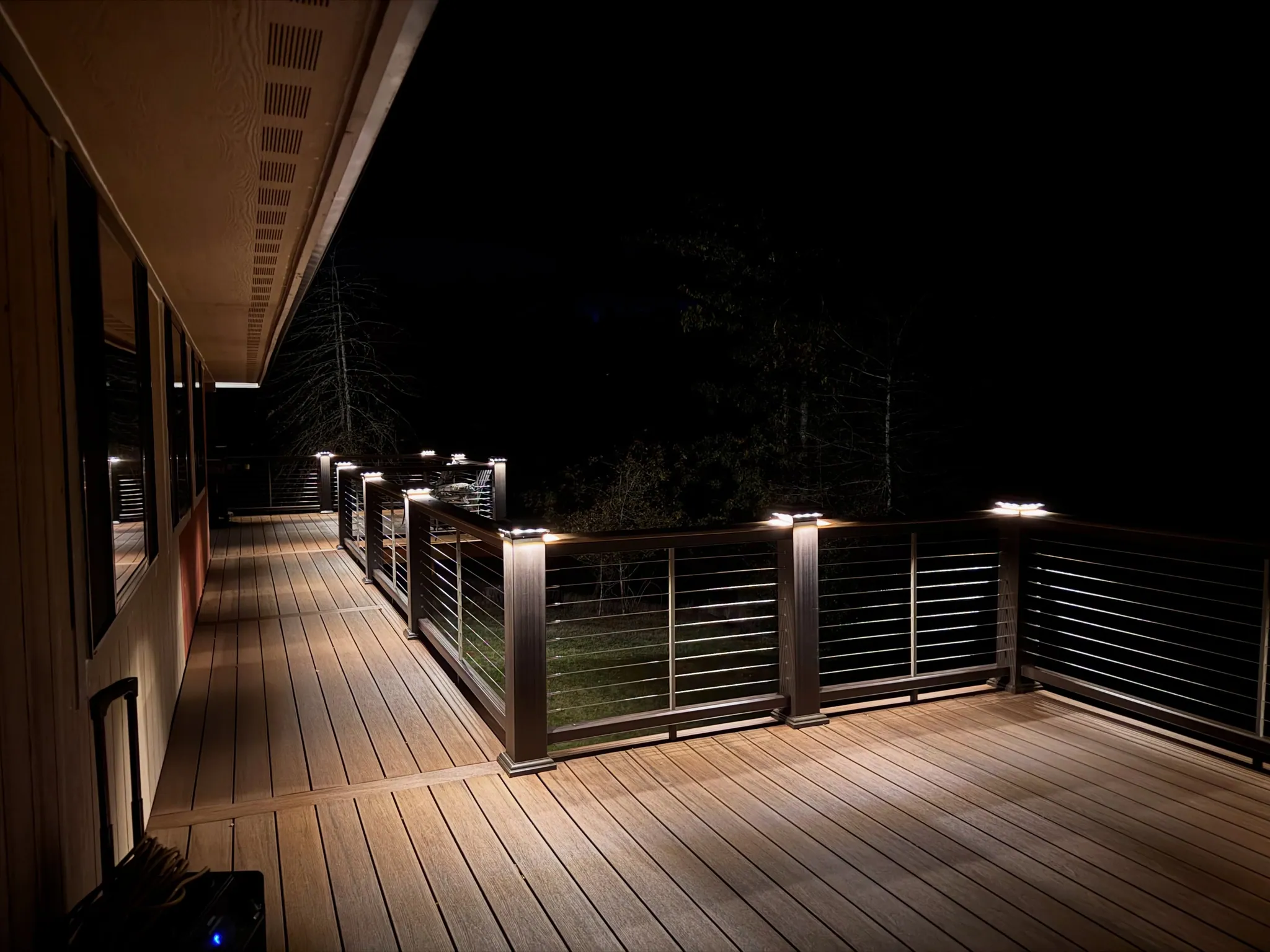 A long TimberTech custom deck at night, post-cap lights glowing along the cable railing